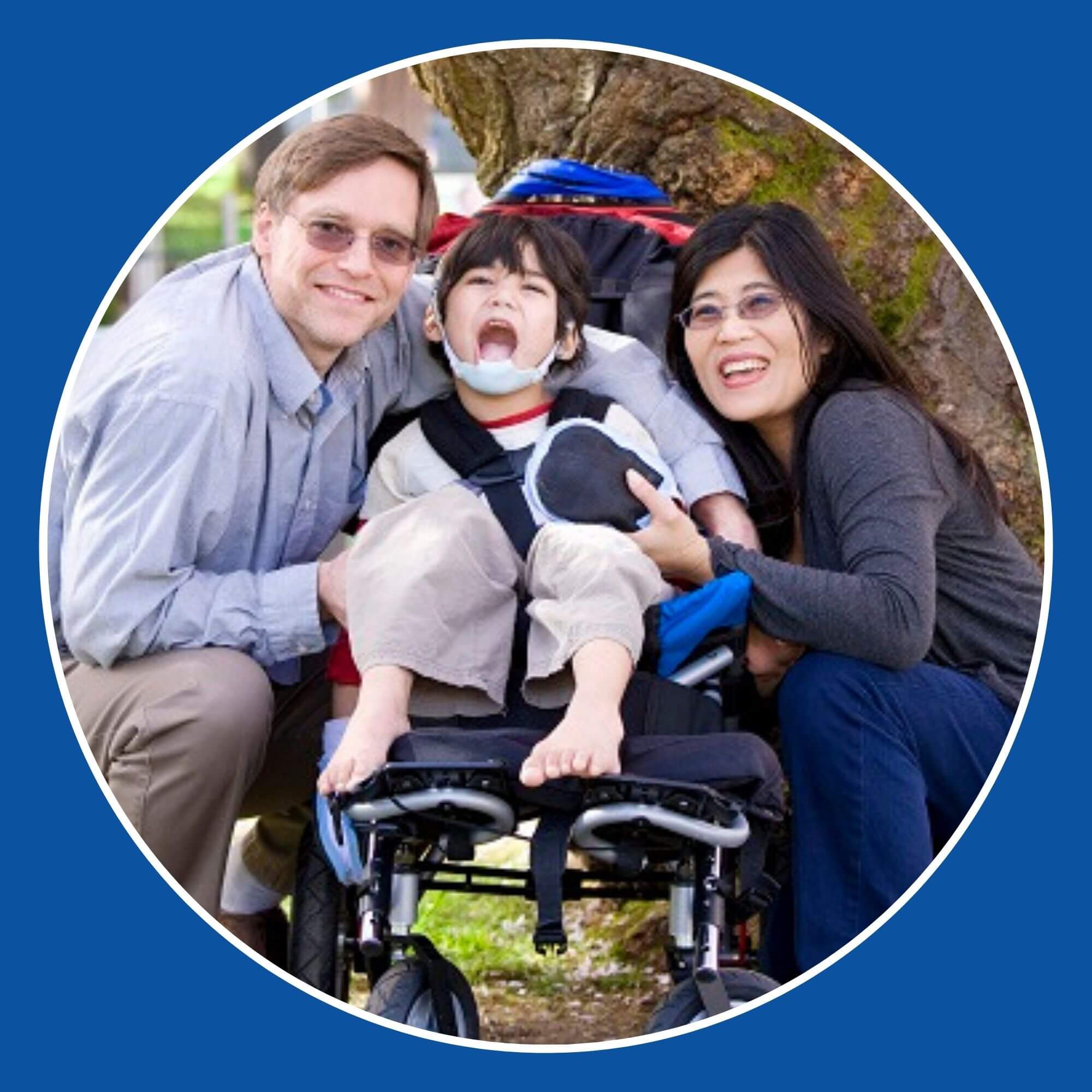 A photo of a Mum and Dad with their son who is in a wheelchair, out in the fresh air together next to a tree.