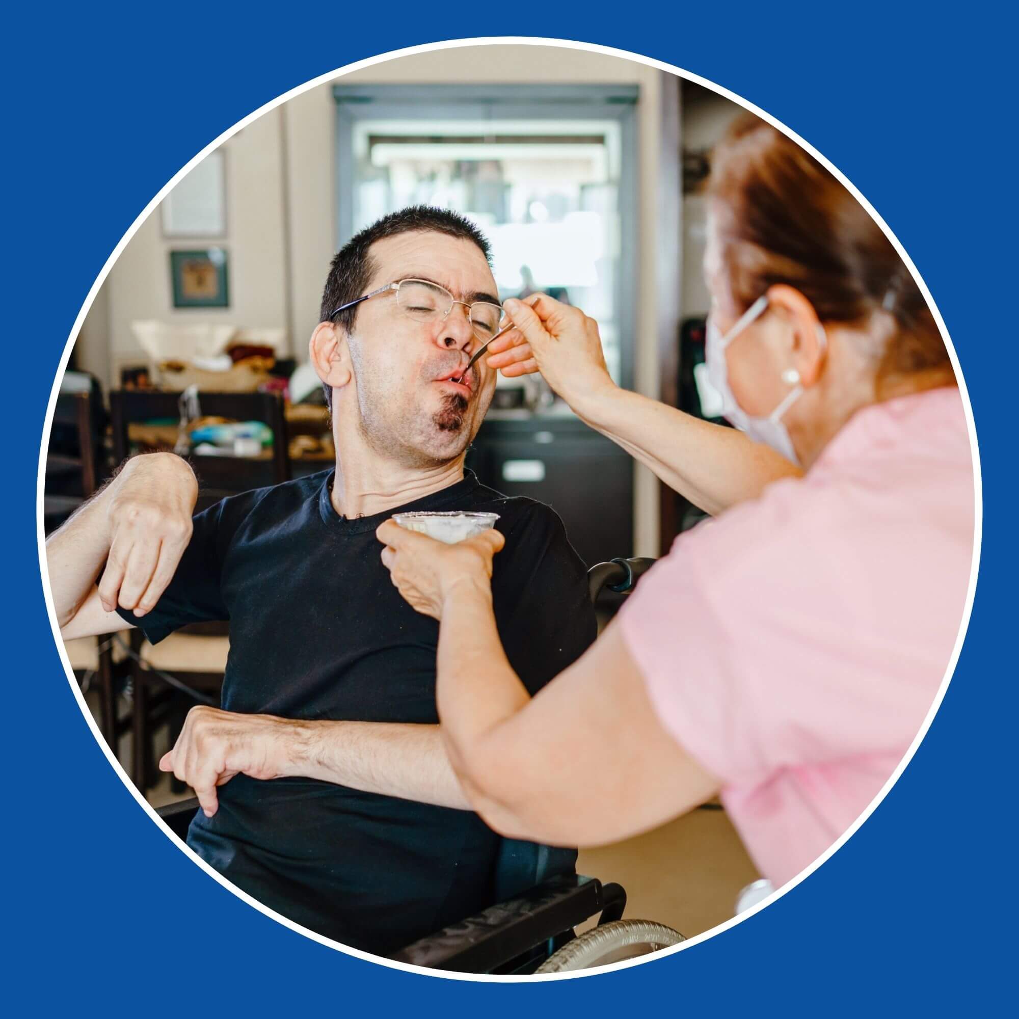 A Personal Assistant helping to feed a gentleman with a disability in a wheelchair (Image from iStock-1255038289)