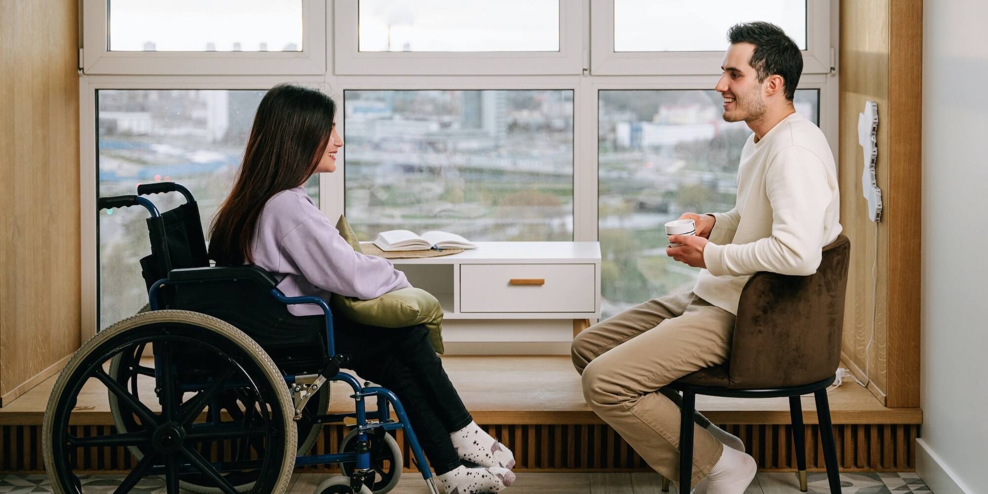 A PA chatting with a young lady in a wheelchair over coffee (image from Pexels by Ivan Samkov)